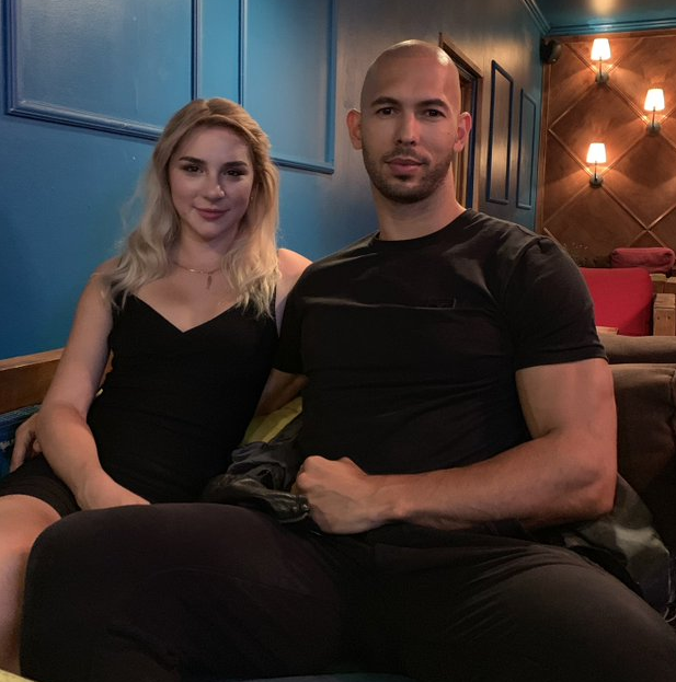 Mikhaila Peterson sitting down being held by Andrew Tate next to a blue wall wearing black.